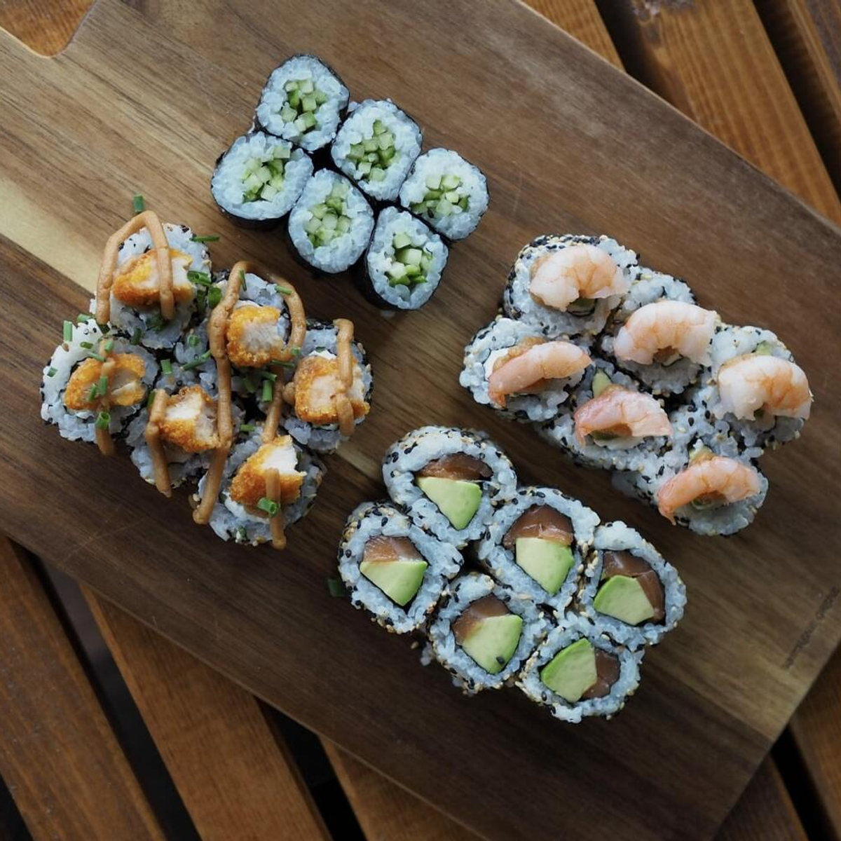Soul Maki Menü auf einem Holzbrett: Crispy Chicken Roll, Garnelen Roll, Lachs Avocado California Maki und Gurken Maki